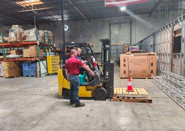 Instructor coaching a forklift operator during hands-on certification training in a warehouse